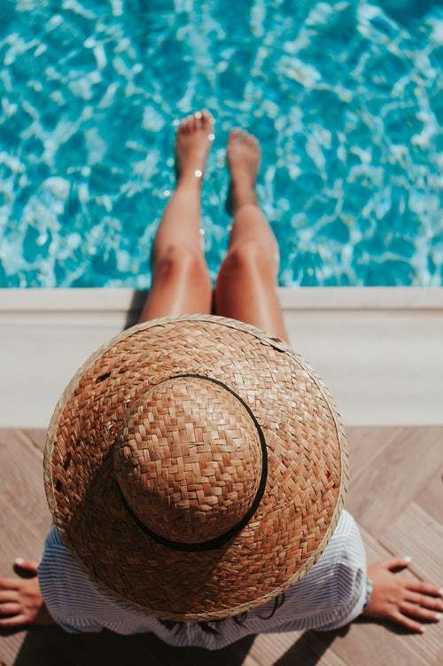 Femme avec chapeau et les pieds dans la piscine